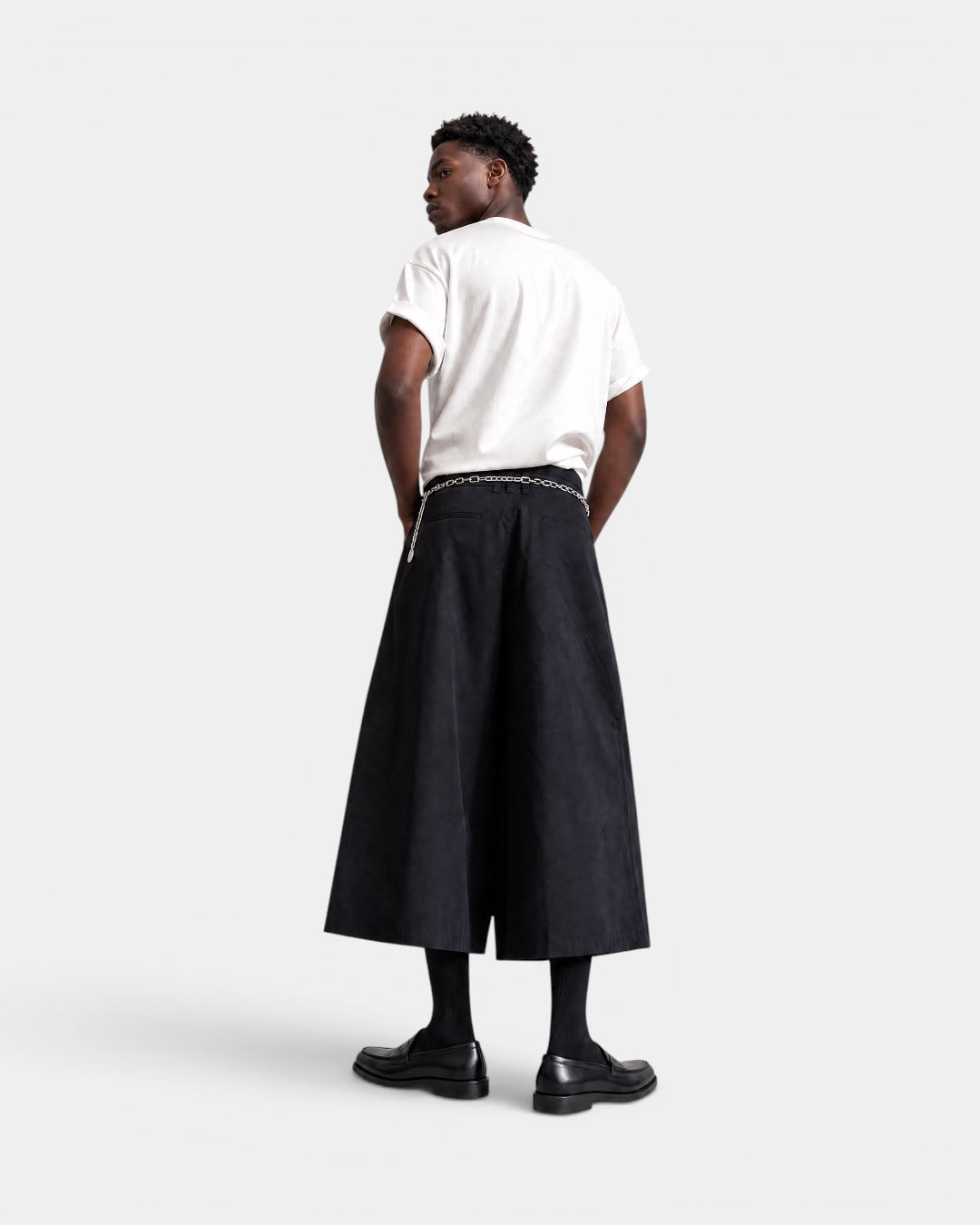 Nameless black A-line culottes with a silver chain belt, worn by a man with a white t-shirt and black loafers.