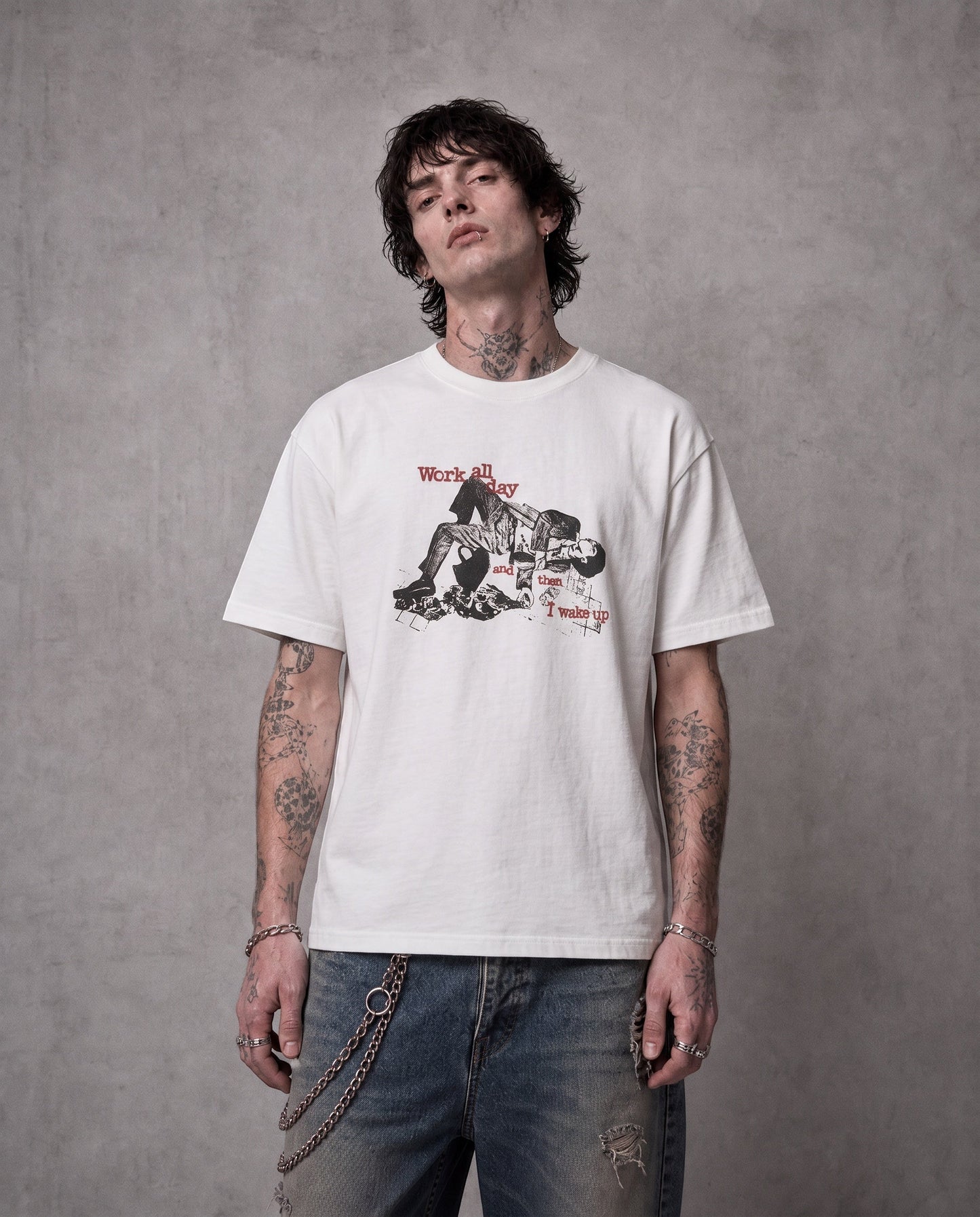 ANTIPROMINDのWORK ALL DAYグラフィックTシャツを着用した男性。柔らかな天竺コットン素材のホワイトTシャツにヴィンテージ風プリントが施されている。