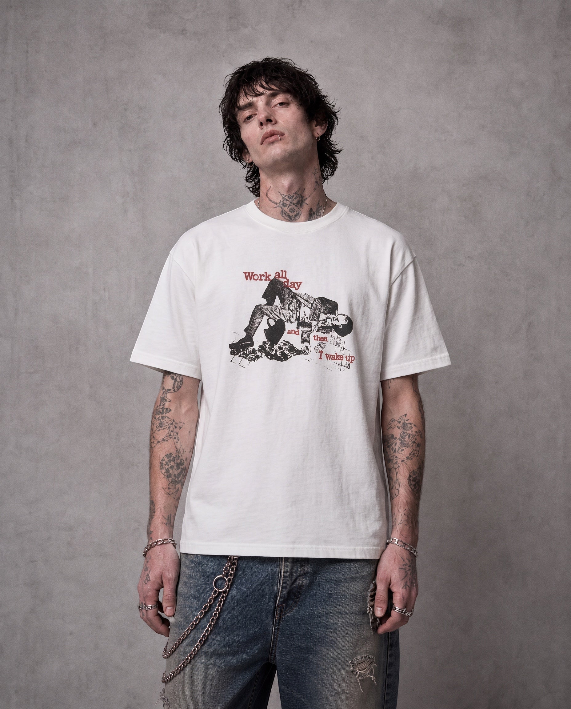 ANTIPROMINDのWORK ALL DAYグラフィックTシャツを着用した男性。柔らかな天竺コットン素材のホワイトTシャツにヴィンテージ風プリントが施されている。