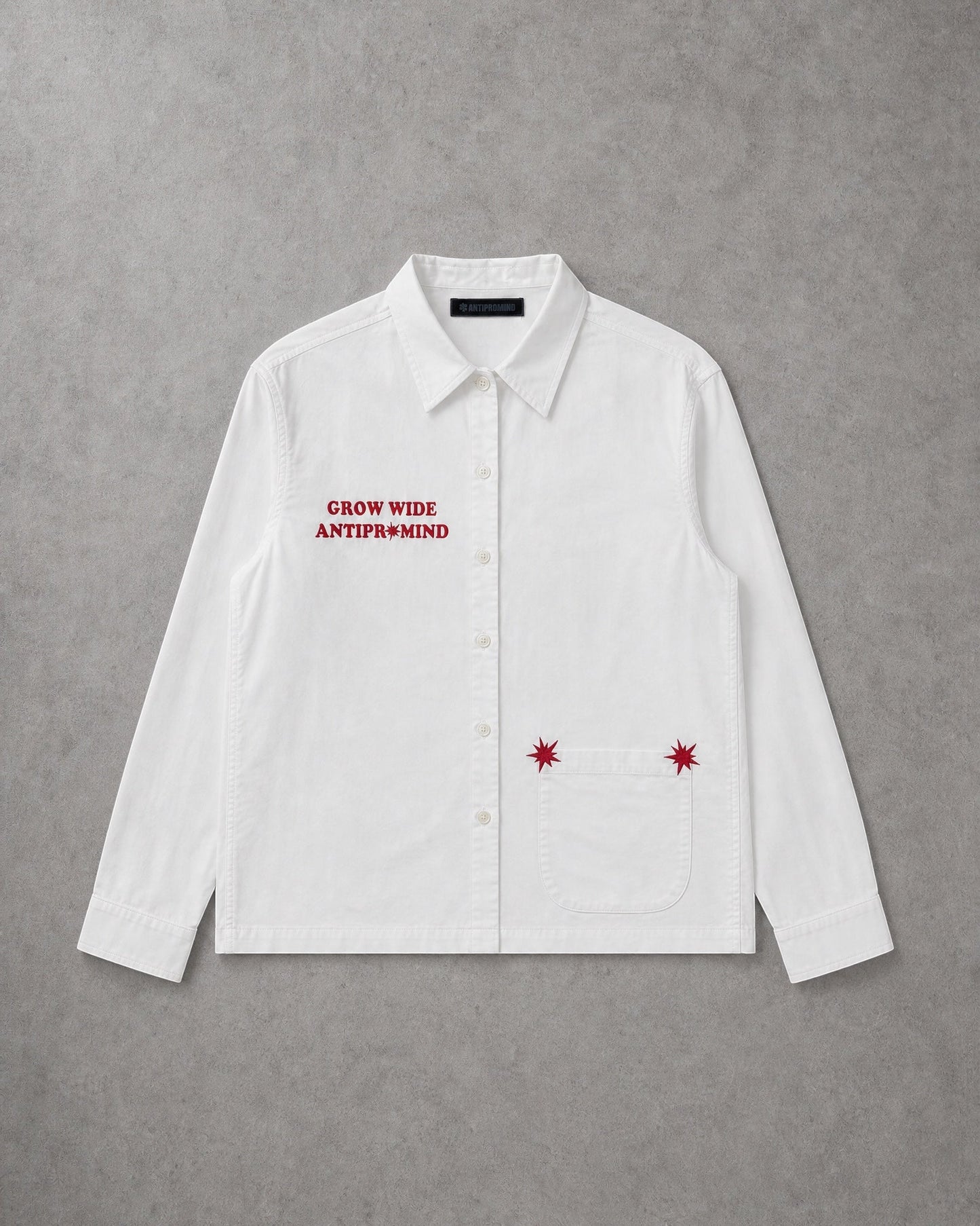 ANTIPROMINDの白いコットン製オープンカラーシャツ。胸元の赤いシリコンプリントとポケットの刺繍が特徴のショート丈スリムフィットシャツ。