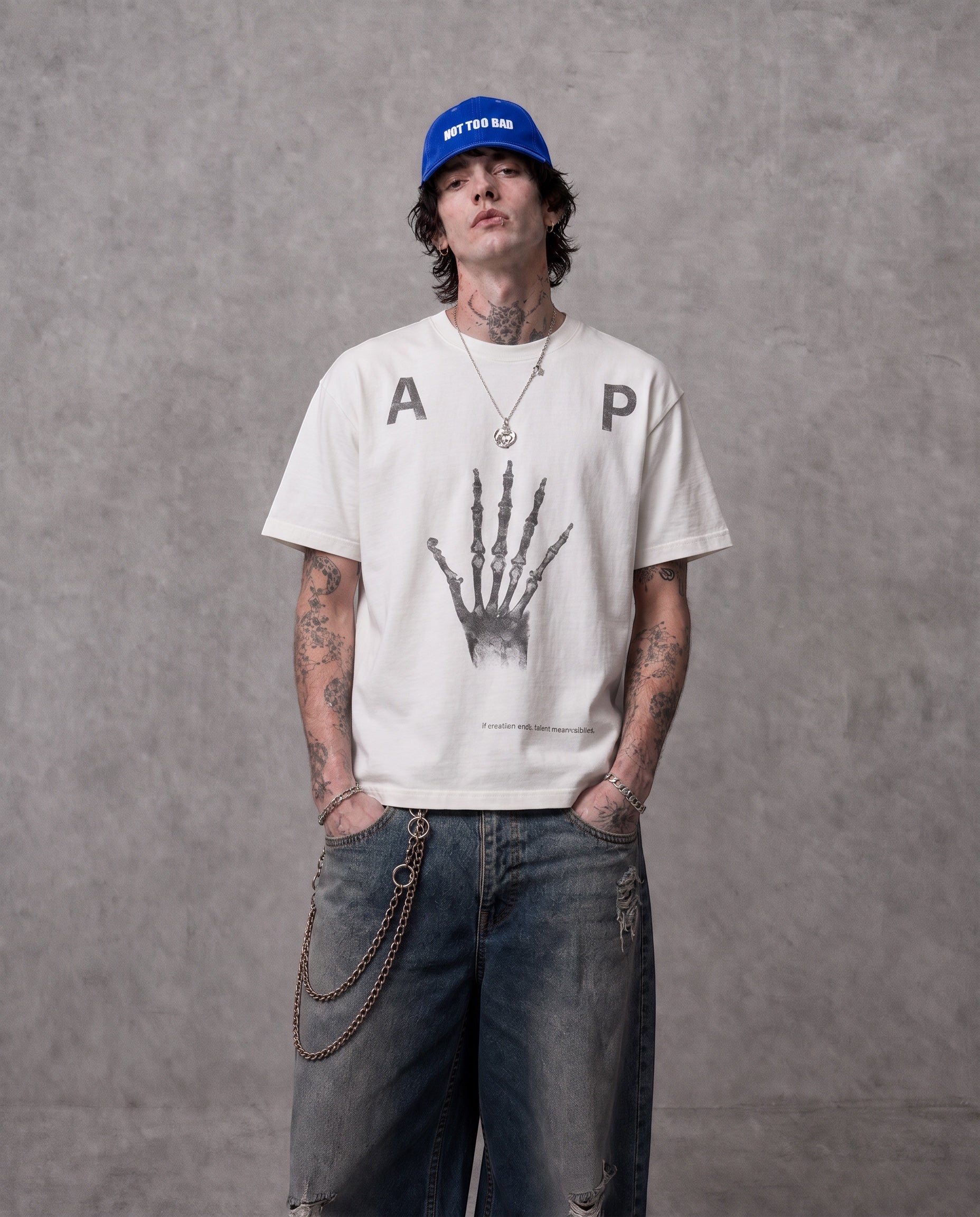 ANTIPROMINDのスケルトンハンドグラフィックがプリントされたホワイトの天竺コットンTシャツを着用した男性モデル