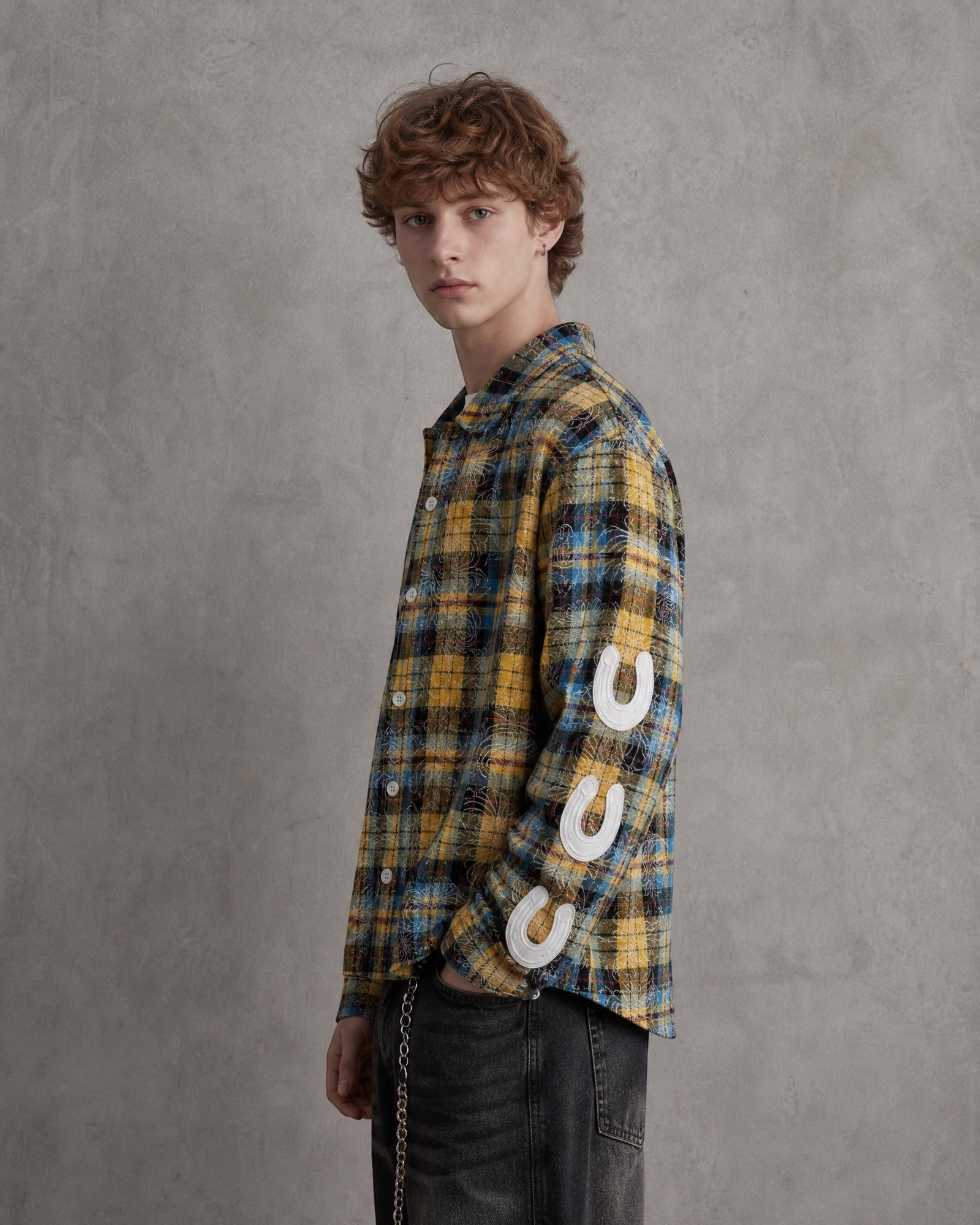 ANTIPROMINDのイエローチェック柄シャツ。袖にPU製ホースシューパーツをあしらったスリムフィットのコットンシャツを着用した男性モデル。