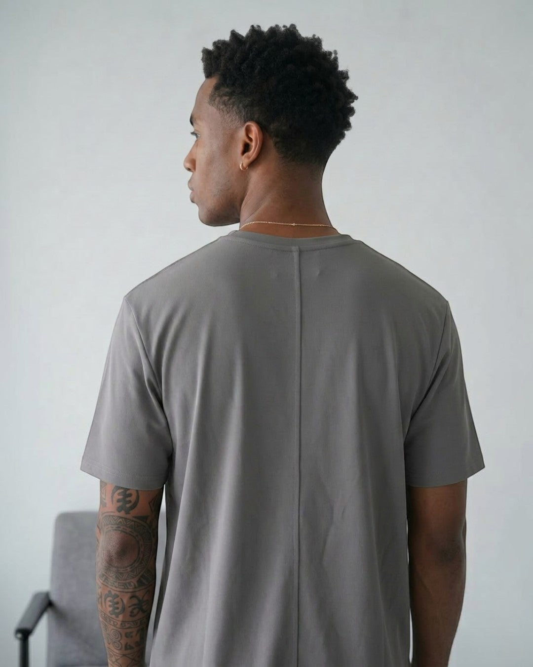 BASISのトライアセテート素材のグレー無地Tシャツ。リラックスフィット、クルーネック、サイドスリット、バータックが特徴。男性着用。
