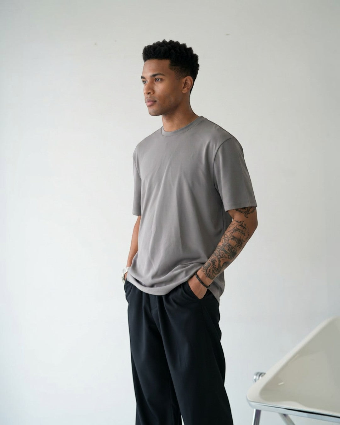 BASISのトライアセテート素材のグレー半袖Tシャツ。リラックスフィット、クルーネック、サイドスリットが特徴。男性モデル着用。