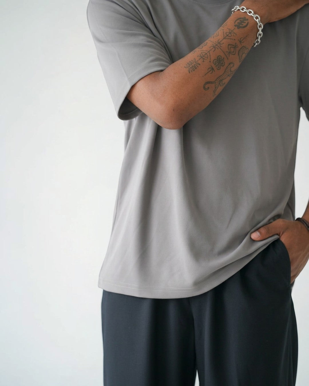BASISのグレーのトライアセテート半袖Tシャツ。リラックスフィット、クルーネック、サイドスリット。男性着用。