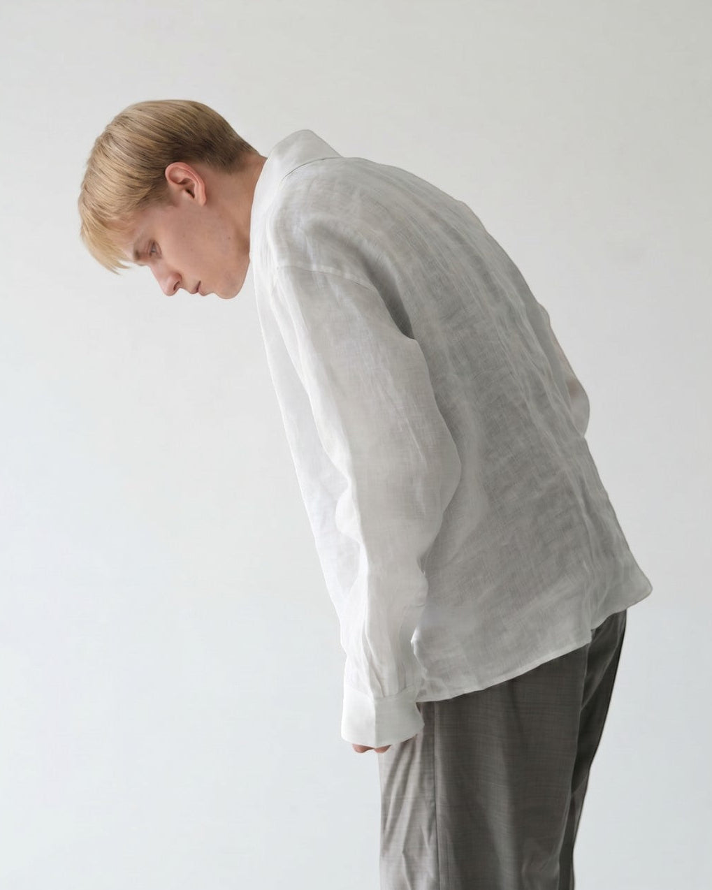 BASISの白いリネン長袖シャツ。ゆったりとしたシルエットとVネックが特徴。男性モデル着用。
