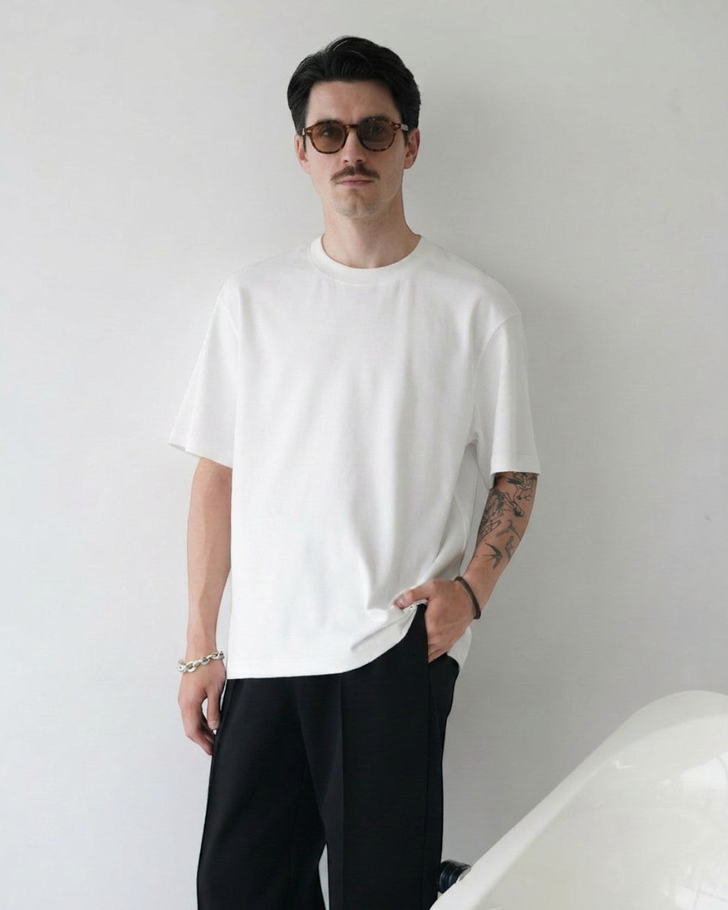 BASISMの白いトライアセテート半袖Tシャツ。リラックスフィット、クルーネック、サイドスリット。男性モデル着用。