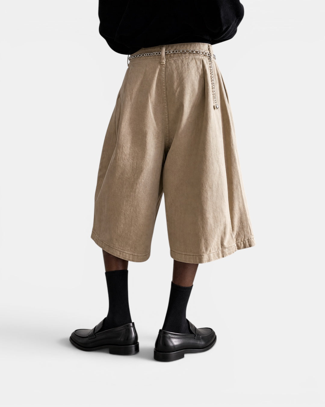 NAMELESS beige three-dimensional tailored wide-leg shorts with a silver chain belt, worn with black socks and loafers.