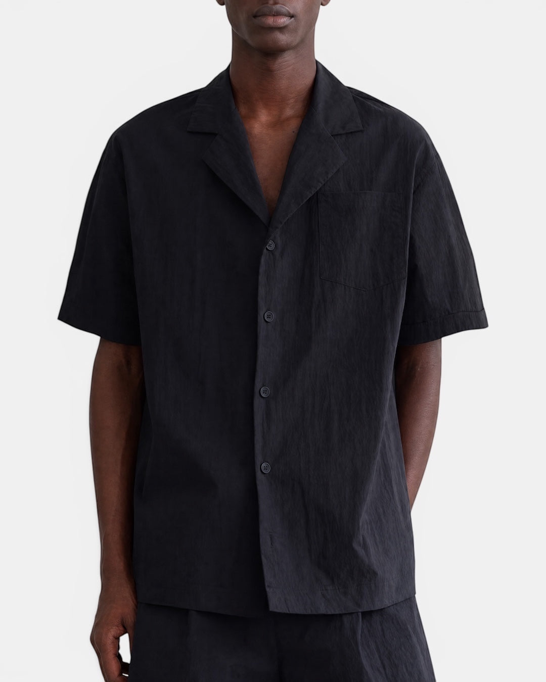 Nameless black short-sleeve Cuban-collar shirt with a chest pocket and button front, made from textured fabric.