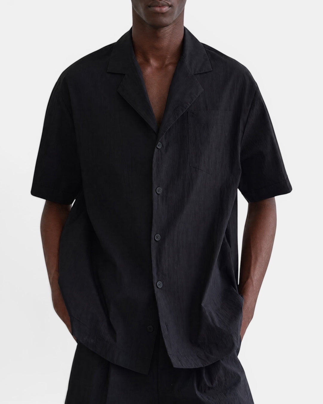 Nameless black short-sleeve Cuban collar shirt with a chest pocket and button front, styled by a man.