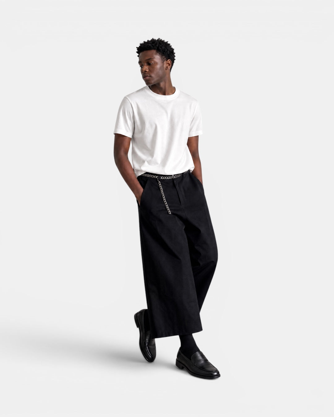 Nameless black wide-leg culottes with chain belt detail, worn by a man in a white t-shirt and black loafers.