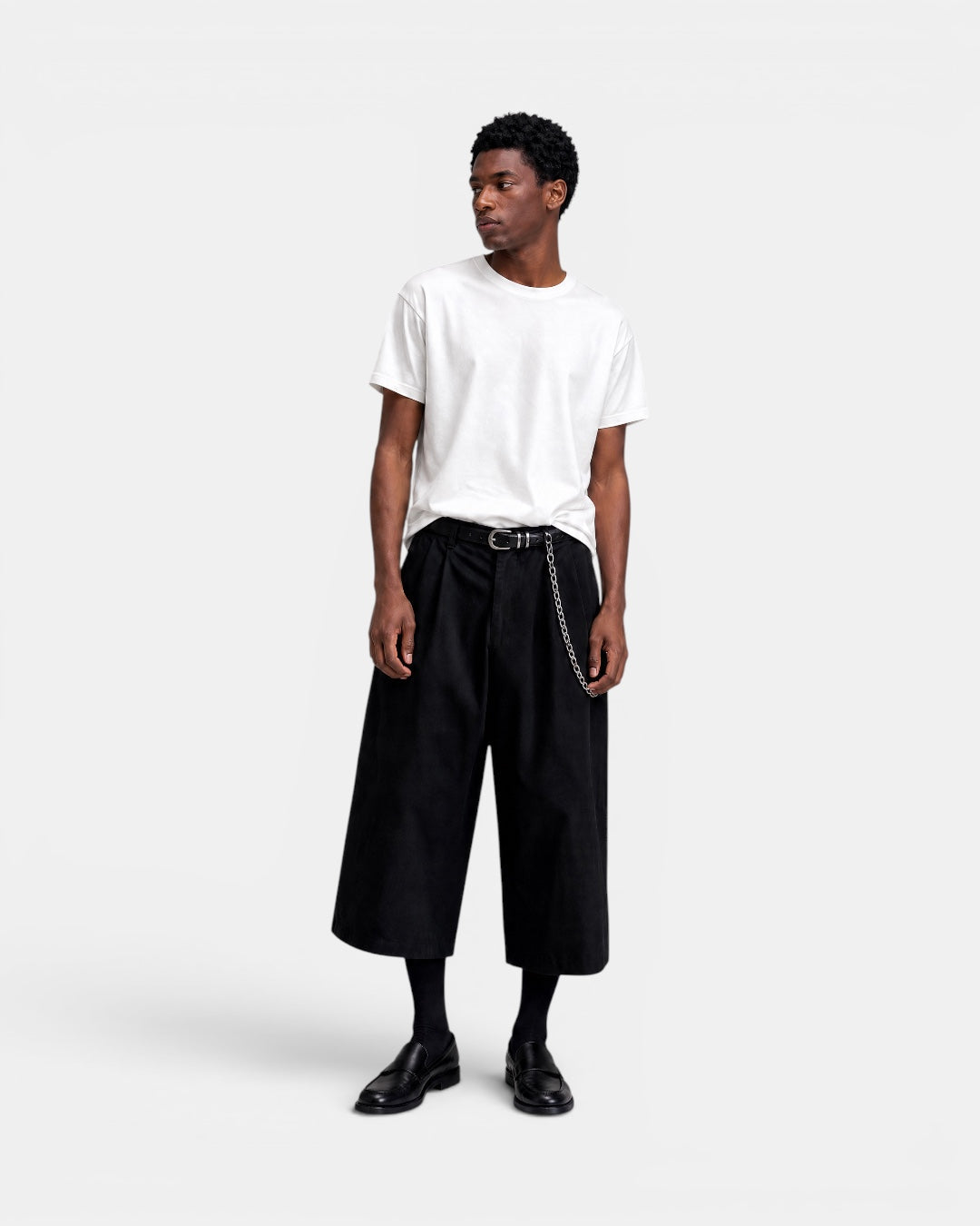 Nameless black wide-leg culottes with pleats and a silver chain belt, worn by a man with a white t-shirt and black loafers.