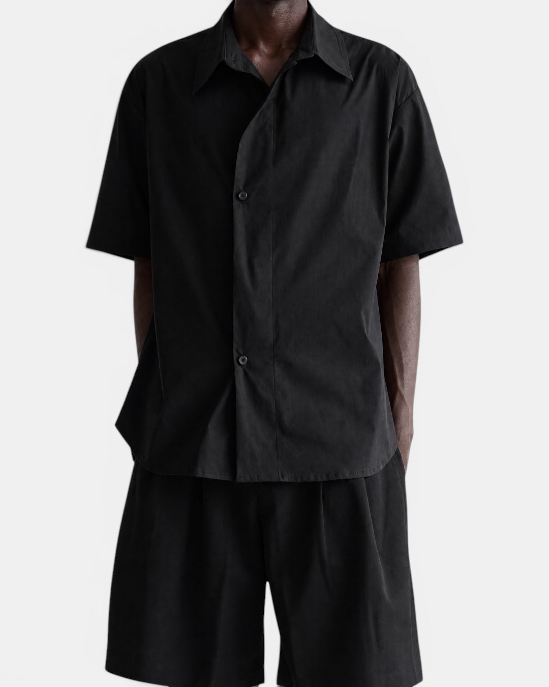 Nameless black short-sleeved shirt with pointed collar and slanted placket, worn by a man.