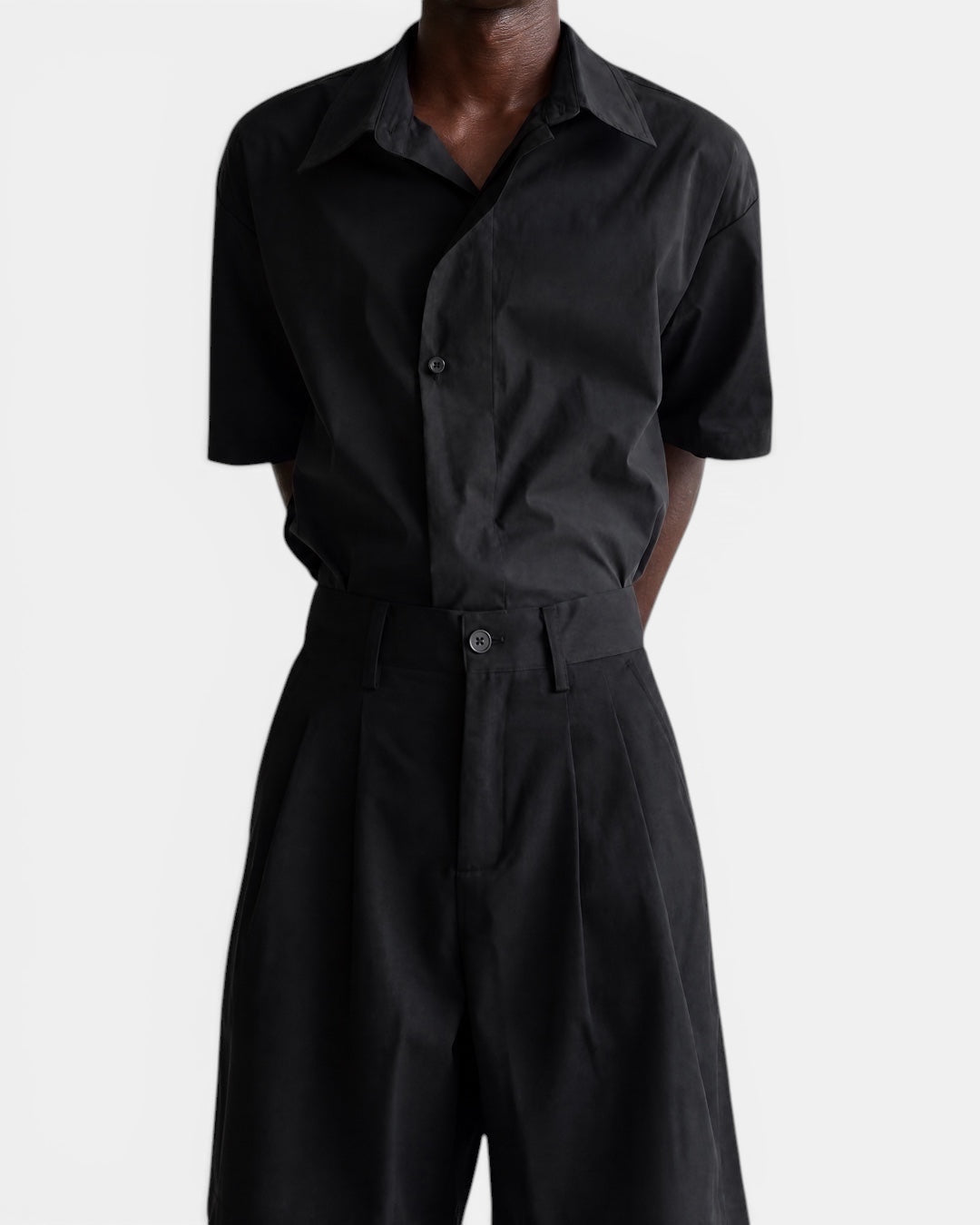 Nameless black short-sleeved cotton shirt with pointed collar and slanted placket, worn by a model.