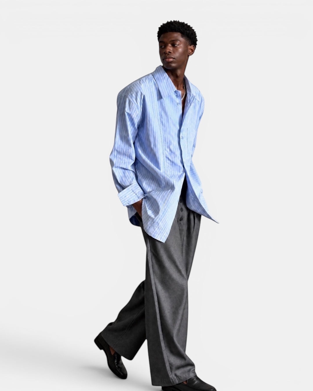 Nameless light blue striped long-sleeved collared shirt worn by a man with hands in pockets.