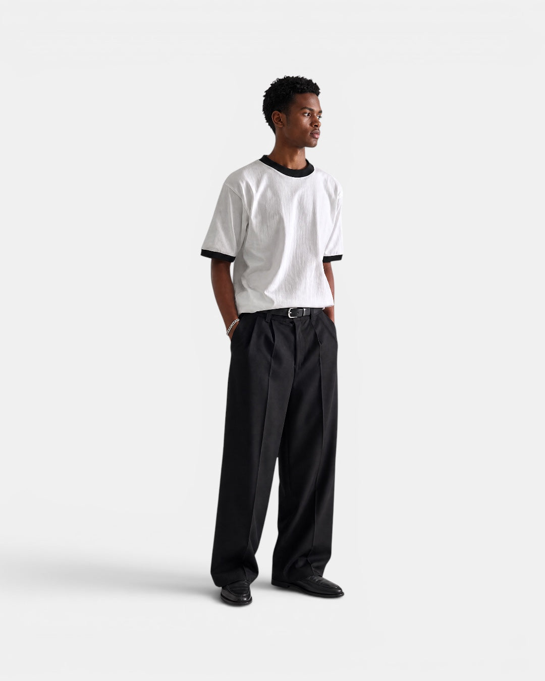 Nameless white cotton t-shirt with black trim on collar and sleeves, worn by a man with black trousers.