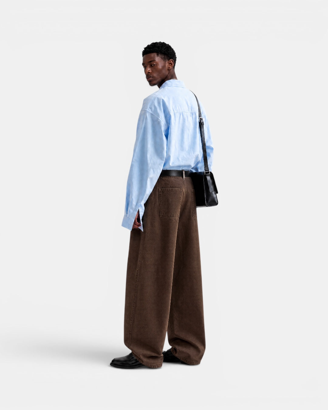 Nameless light blue solid-color long-sleeved cotton shirt worn by a man with brown wide-leg pants and a black crossbody bag.