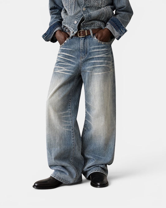 NAMELESS light wash distressed denim wide-leg jeans with whiskering and fading. Model wears a brown belt and black shoes.